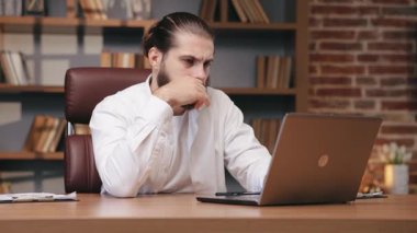 Saçı arkadan bağlanmış, rahat ofisinde dizüstü bilgisayarla çalışan ciddi bir adam. Beyaz gömlekli bir adamın portresi dizüstü bilgisayara bakıyor, iş projesini düşünüyor. İş kavramı.