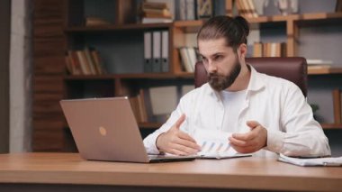 Kendine güvenen iş adamı merkez ofiste video konferansı yapıyor. Orta yaşlı yöneticinin online konuşması, baş parmağını kaldırması, yumruklarını kaldırması, harekete geçmesi. İş, uzak çalışma konsepti.