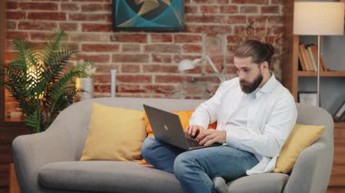 Beyaz gömlekli, odaklanmış beyaz bir adam kanepeye oturmuş laptopunda yoğun bir bakışla yazı yazıyor. Dönüm noktasından sonra hafif bir gülümseme beliriyor. Yaratıcı çözüm üzerinde çalışırken parlak fikri deneyimlemek.