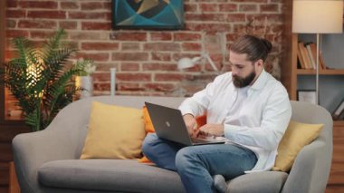 Beyaz gömlekli ve kot pantolonlu sinirli bir beyaz adam koltukta oturmuş bilgisayarın tuşlarına basıyor. Gergin bir duruşla öne doğru eğiliyor. Teknik sorunlarla uğraşırken öfkesini ifade etmek. Bağırarak..