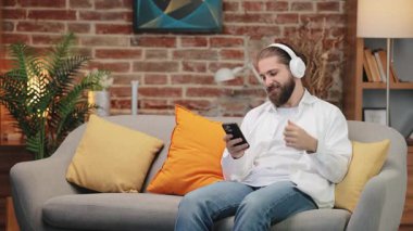 Kafkasyalı rahat bir adam kanepeye oturmuş hava gitarı çalıyormuş gibi yapan renkli yastıklarla çevrili. Müzikle uğraşırken beyaz gömlek ve kot pantolon giyiyor. Rahat evde ritmin tadını çıkarıyorum..