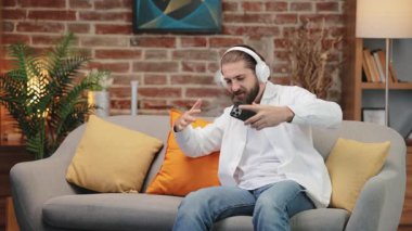 Heyecanlı, kulaklıklı, dans eden, evde şarkı ritmiyle titreşen hippi bir erkek. Sıradan kıyafetler giymiş sakallı bir adam, rahat koltukta hareketli bir şekilde otururken müziğin tadını çıkarıyor. Müzik, titreşim konsepti.