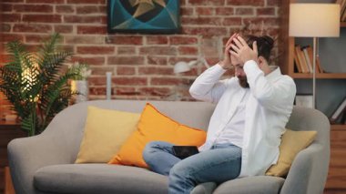 Beyaz gömlekli harap olmuş beyaz adam koltukta oturuyor ve telefonu kucağına düşmüş. Duygusal şoktan sonra iki elinle yüzünü kapatıyorsun. Sinir bozucu mesajı okuduktan hemen sonra telefonu düşürme.