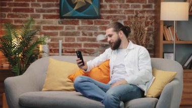 Rahat giyimli, dost canlısı beyaz bir adam kanepeye oturmuş elinde akıllı bir telefonla onayını veriyor. Neşeli bir gülümsemeyle hafifçe eğiliyor. Arkadaşla gündelik sohbetin keyfini çıkarıyorum..