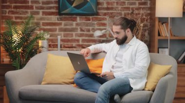 Kanepede bağdaş kurmuş oturan yakışıklı beyaz adam ciddi suratlı dizüstü bilgisayara bakıyor. Mesajı düşünürken çeneyi tutmak. En iyi cevabı düşünüp iletişim zorluğuyla yüzleşmek.