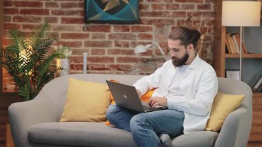 Yazdıktan sonra kanepeye oturmuş laptopun kapağını kapatan beyaz bir adam. Görevi tamamlıyorum. E- posta gönderiliyor ya da form gönderiliyor. Rahat ortamda iş oturumunu bitiriyorum. Uzaktan iletişim konsepti.