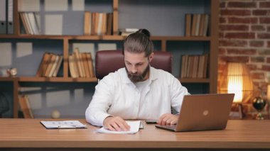 Masadaki kağıtlara yan gözle bakarken dikkati dağılmış beyaz bir adam kulağını tırmalıyor. Belgelere göz atmak ya da basılı bilgileri gözden geçirmek. Uzaktan çalışmak ve hafif kafa karışıklığıyla görevleri idare etmek.
