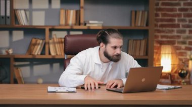 Kafası karışmış beyaz bir adam dizüstü bilgisayara doğru eğilmiş gergin bir suratla akıllı telefon tutuyor. Doğru kelimeleri bulmak ya da cevap vermeden önce tereddüt etmek. Sohbet sırasında ya da e-posta yanıtında belirsizlik ya da sıkışma.