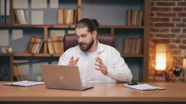 Beyaz tişörtlü, elinde not panosu olan ve parmak izi tablosuna işaret eden konsantre beyaz bir adam. İstatistikleri sunmak ya da verileri açıklamak. Çevrimiçi toplantı sırasında sanal rapor ya da sunum projesi yürütülüyor