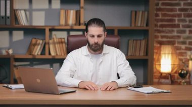 Masada oturan kendine güvenen beyaz adam göğsünün önünde kollarını kavuşturuyor. Teklifi reddetmek ya da şiddetle karşı çıkmak. Sanal iletişim sırasında net reddetme veya katı sınırlar koymak.
