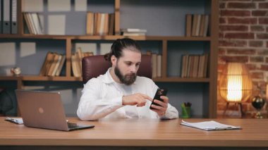 Masada otururken akıllı telefonu dinleyen, sakallı, sıkılmış, beyaz bir adam. Amaçsız besleme yaparak zaman öldürmek. İşten ve sessiz ofis ortamındaki görevlerden uzak durmak..