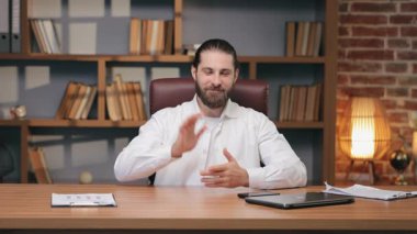 Kameranın önünde otururken gülümseyen beyaz adam elini kaldırıyor. İş arkadaşlarını selamlamak ya da video görüşmesi sırasında veda etmek. Sanal toplantıya ya da uzak sohbet oturumuna sımsıkı bağlanılıyor.