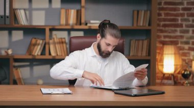 Masada otururken kalın klasörleri hızla karıştıran kararlı beyaz adam. Acilen kayıp belge ya da detaylar aranıyor. Yoğun görev sırasında evrak işlerine yoğunlaşmak.