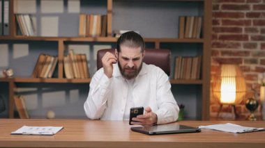 Tiksindirici sakallı adam tek eliyle alnını kapatırken akıllı telefona bakıyor. Rahatsız edici bir şey gördükten sonra şoke olmuş. Nahoş görüntüye veya beklenmedik içeriğe güçlü tepki.