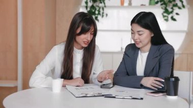 Yanında kahve fincanları ve akıllı telefonlar ile yuvarlak masada otururken, parmak izi çizelgelerini yakından inceleyen iki iş arkadaşı. Odaklanmış ofis toplantısında strateji üzerinde işbirliği yapmak veya analizleri gözden geçirmek.