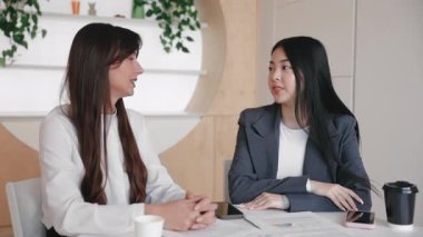 Beyaz gömlekli arkadaş canlısı bir kadın masanın karşısına elini uzatırken meslektaşı hafif bir tebessümle tereddüt ediyor. İş görüşmesi sırasında tartışmayı sonlandırmaya ya da selamlama sunmaya hazırlanılıyor.