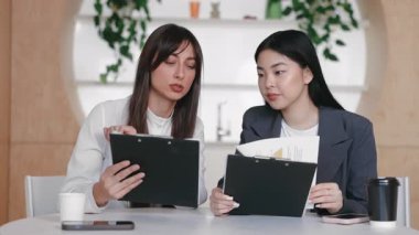 Ortak masaya hafifçe yaslanarak panodaki yazılı verileri analiz eden iki odaklı meslektaşım. Çizelge sonuçlarını tartışmak ya da sessiz ofiste proje stratejisini yanında paket servis bardaklarıyla hizalamak