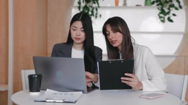 İki odaklı kadın açık dizüstü bilgisayar ve panoyla birlikte verileri gözden geçirirken birlikte çalışıyor. Organize ofiste otururken sezgileri paylaşmak ya da sunumu tamamlamak. Veriler karşılaştırılıyor.