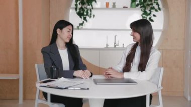 İki kadın birbirine saygı ve sakin bir gülümsemeyle bakarken sıcak bir şekilde el sıkışıyor. Modern çalışma sahasında otururken verimli toplantının sonu veya başarılı müzakerelerin sonu.