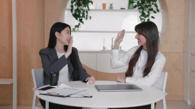 Sırıtkan meslektaşlar, evrak ve aletlerle masada otururken beşlik çakıyor. Takım çalışmasının başarısını kutlamak ya da parlak modern çalışma alanında paylaşılan heyecanla görevi sonuçlandırmak.