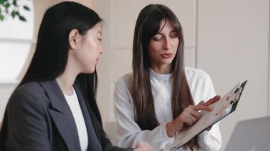 Esmer kadın dosya detaylarını açıklarken meslektaşı da onu dikkatle dinliyor. Dostça ve verimli toplantı sırasında iş stratejisi veya proje verilerinin gözden geçirilmesi