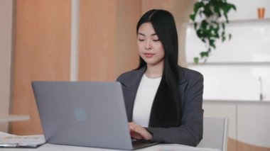 Sakin bir çalışma sırasında laptopta yazarken gülümseyen neşeli Asyalı kadın. E- posta giriliyor ya da meslektaşınıza yanıt verilirken, temiz bir mesleki ortamda meşgul ve üretken olunuyor.