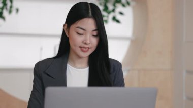 Video toplantısı ya da sanal sunum sırasında dizüstü bilgisayarla konuşan Asyalı bir kadın. Uzaktan işbirliğine aktif olarak katılmak ya da ofis kurulumunda güvenilir rapor vermek.