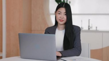 Heyecanlı Asyalı kadın başarıyı kutlarken yumruğunu kaldırıyor ve dizüstü bilgisayarın yanında gülümsüyor. Harika haberler aldıktan ya da uzak çalışma oturumunda kilometre taşı elde ettikten sonra sevinçle tepki vermek.