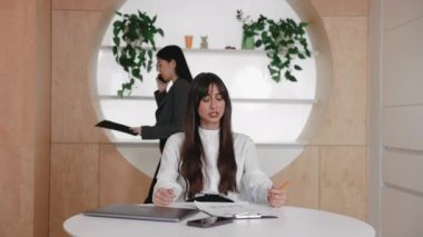 Stresli, beyaz bir kadın masasında oturmuş konsantre olmaya çalışırken hayal kırıklığı içinde başını tutuyor. İş arkadaşı telefonda konuşuyor ve panoyu tutuyor. Gürültülü çalışma alanına odaklanmak için mücadele