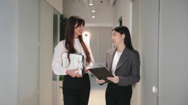 Elinde dosyalar olan çekici beyaz bir kadın ve gri ceketli bir meslektaşla koridorda yürüyor. İş fikirlerini tartışmak ya da toplantı planlamak. Ofise giderken düşüncelerini paylaşmak.