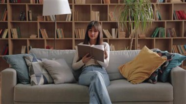 Çekici beyaz kadın kanepenin üzerinde bacak bacak üstüne atıyor ve kitabı tutarken özenle yukarı bakıyor. Yastıklar ve kitaplarla çevrili huzurlu bir odada pasajı yansıtmak ya da hikaye sahnesi hayal etmek..