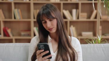 Kafkasyalı kadın başını hafifçe eğiyor, tepkimeye girerken şüpheci bir ifade sergiliyor, yumuşak kanepede parlak bir odada oturuyor. Hayal kırıklığı yaratan mesajı okuduktan sonra düşünceli bir kadın kaşlarını kaldırdı..