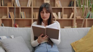 Kafkasyalı ilginç, çekici bir kadın kitabı açık tutuyor ve yukarı bakarken çenesine dokunuyor. Kitap raflarıyla çevrili rahat bir odada kanepede otururken içeriği düşünmek ya da fikirleri analiz etmek.