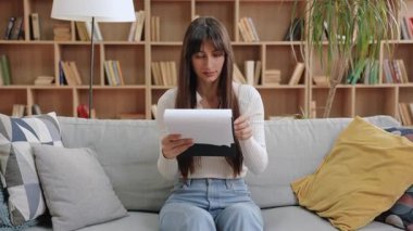 Kendine güveni tam, beyaz bir kadın elinde raporuyla kanepede otururken hafifçe gülümsüyor. Kağıtları gözden geçirmek ya da kitap rafları ve kapalı alan bitkileriyle aydınlatma odasında sunuma hazırlanmak.