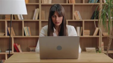 Bilgisayarı kapatan beyaz bir kadın ve parlak odada alnına nazikçe masaj yapan bir kadın. Uzaktan kumandayı bitirmek ve büyük ahşap bir rafın yanında otururken tükenmiş hissetmek. Modern teknoloji