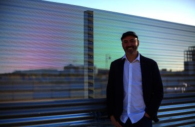 Zarif, olgun bir adam sakin bir şekilde endüstriyel şehir ortamında kameraya bakıyor.