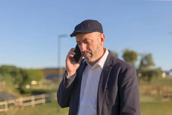 Resmi giyinmiş bir iş adamı, açık havada, güzel bir parkta, parlak güneş ışığı altında konuşurken görülüyor. Odaklanmış konuşması, dingin ve doğal çevreyle çelişiyor. Bu da aradaki pürüzsüz dengeyi gösteriyor.