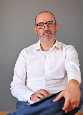 Rahat bir pozisyonda, belgelerini incelerken iş kıyafetleri giyen olgun bir birey. Görüntü profesyonelliği, güveni ve gelişigüzel ama odaklanmış bir ambiyansı yansıtıyor..