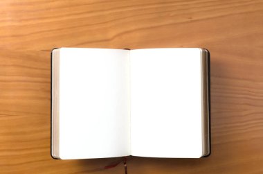 Tahta bir yüzey üzerinde açık bir defter bulunur, içi boş sayfalar yazılmaya ya da çizilmeye hazırdır.