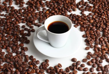 Beyaz fincanda siyah espresso kahvesi, kavrulmuş fasulyelerle çevrili, sıcaklığı, aromayı ve sabah ayinlerinin rahatlığını getiriyor.