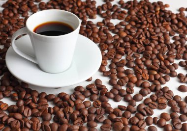 Kızarmış fasulyelerle çevrili beyaz bir fincanda taze demlenmiş siyah espresso kahvesi sıcaklığın ve sabah aromasının özünü yakalıyor.