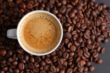 Beyaz espresso fincanı kızarmış kahve çekirdekleri ile çevrili, yukarıdan çekilen zengin doku ve aromayı vurgulamak için.