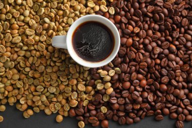 Bir fincan sade espresso kahvenin en üst görüntüsü. Arkaplandaki çiğ ve kavrulmuş kahve çekirdeklerine karşı sanatsal bir ortamda..