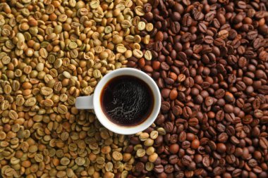Bir fincan sade espresso kahvenin en üst görüntüsü. Arkaplandaki çiğ ve kavrulmuş kahve çekirdeklerine karşı sanatsal bir ortamda..