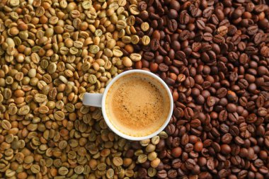 Bir fincan kremalı espresso kahvenin en üst görüntüsü. Arkaplandaki çiğ ve kavrulmuş kahve çekirdeklerine karşı sanatsal bir ortamda..
