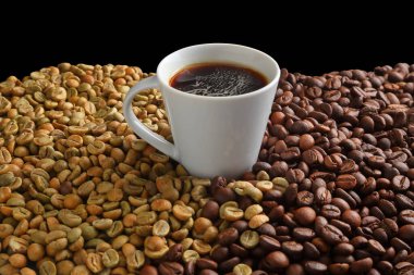 Bir fincan siyah espresso kahve. Arkaplandaki çiğ ve kavrulmuş kahve çekirdeklerinin üzerine serpiştirilmiş..