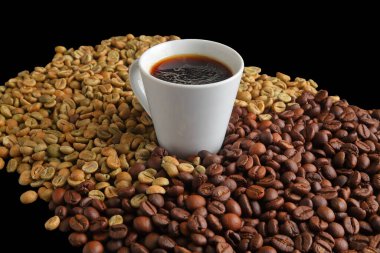 Bir fincan siyah espresso kahve. Arkaplandaki çiğ ve kavrulmuş kahve çekirdeklerinin üzerine serpiştirilmiş..