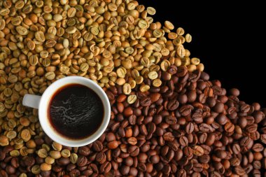 Bir fincan sade espresso kahvenin en üst görüntüsü. Arkaplandaki çiğ ve kavrulmuş kahve çekirdeklerine karşı sanatsal bir ortamda..