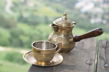 Ahşap bir masada Fincan ile metal bardak ve çay tabağı..