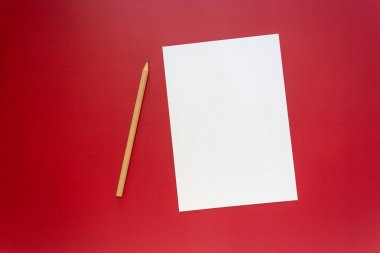 Eğitim, yaratıcılık, yazma ve tasarım ile ilgili kavramlar için koyu kırmızı bir zemin üzerinde beyaz bir kağıt ve ahşap bir kalem dinlenme. 